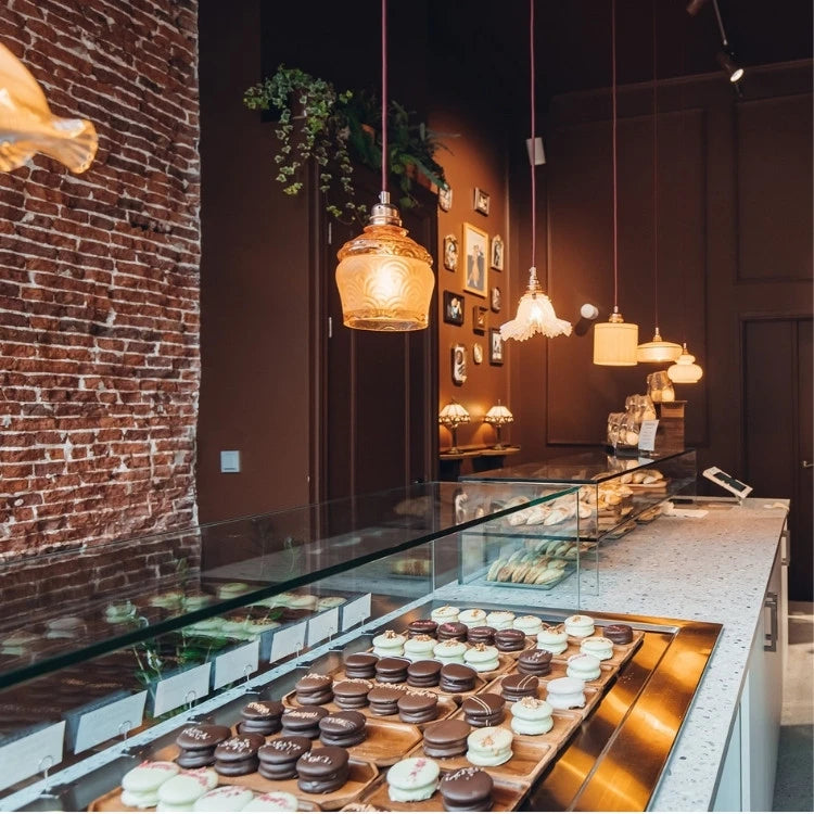winkelinrichting op maat met lichte terrazzo toonbank, glazen patisserievitrine, donkerbruin winkelinterieur en bakstenen muur met warme hanglampen voor luxe patisserie winkelinterieur