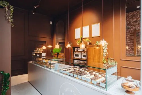 winkelinrichting op maat met lichte toonbank, glazen patisserievitrine en warm bruin horeca winkelinterieur met hanglampen en productpresentatie