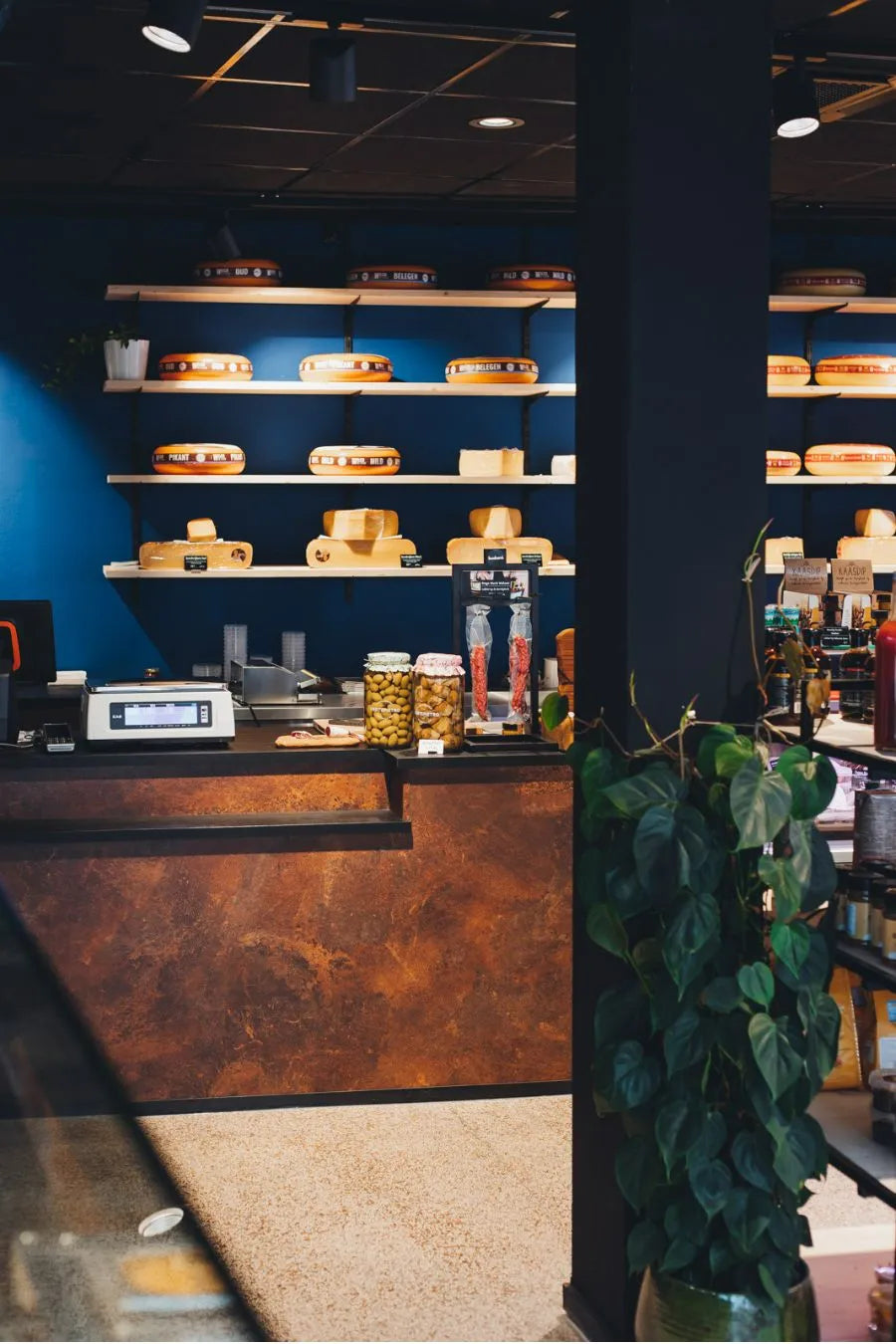 winkelinrichting op maat met roestkleurige toonbank, wandplanken met kaasproductpresentatie en modern speciaalzaak winkelinterieur