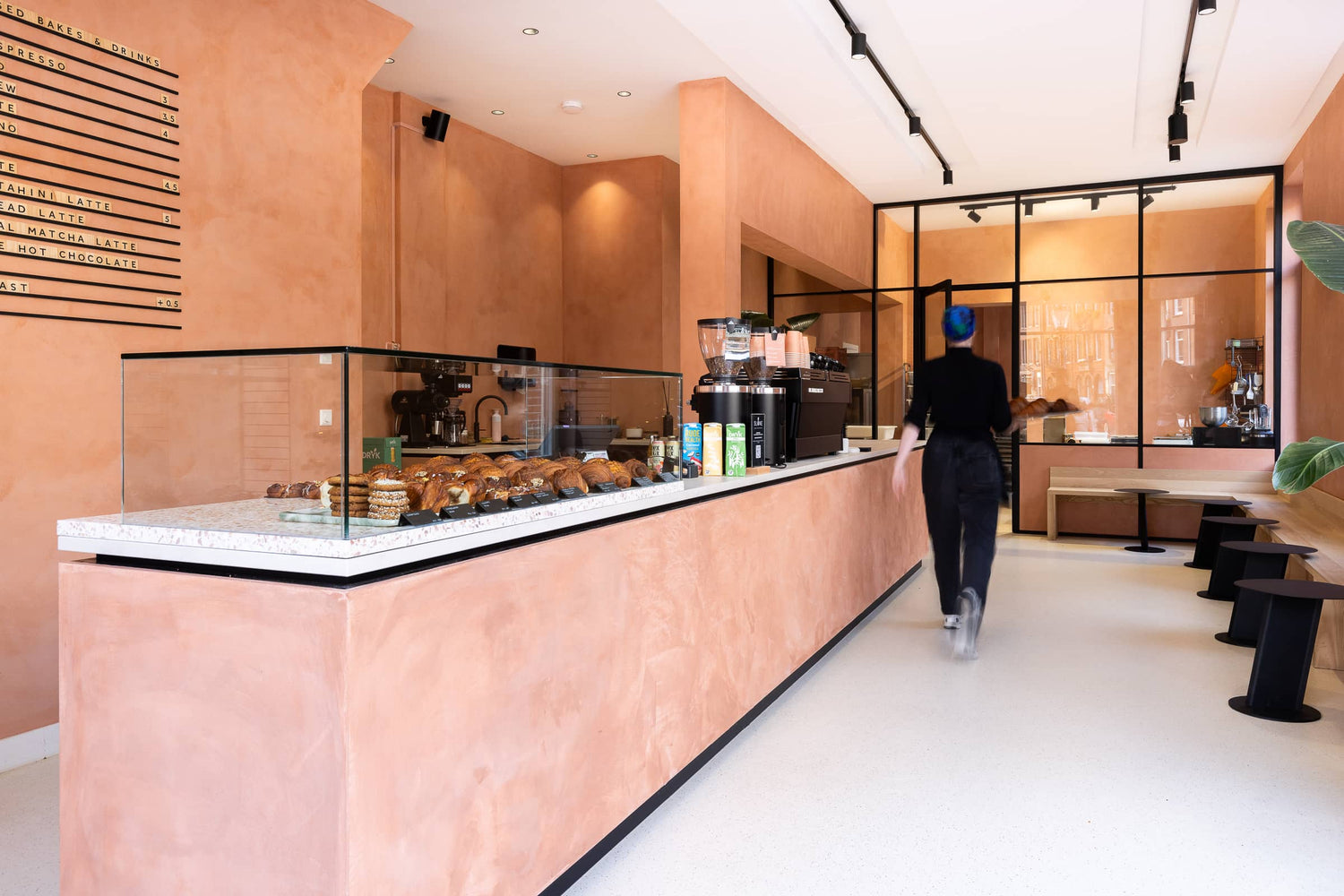 Moderne koffiebar met toonbank, glazen vitrine met vers gebak en open zitgedeelte achter glaswand.