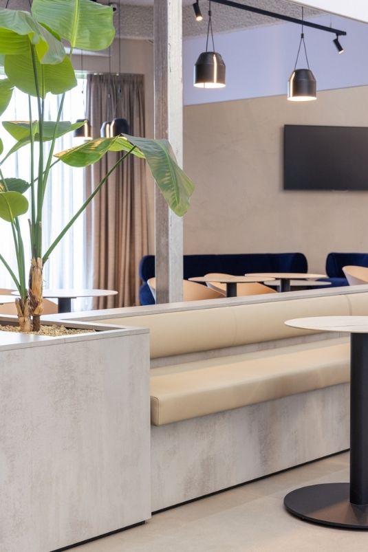 Maatwerk zitbank met tafels en plantenbak in een modern clubhuisinterieur voor sportkantine en leisure inrichting.