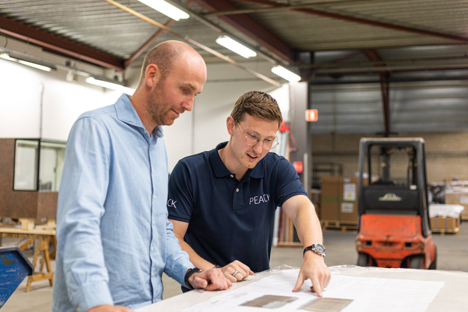 Twee medewerkers van PEACK nemen in de werkplaats een werktekening door.