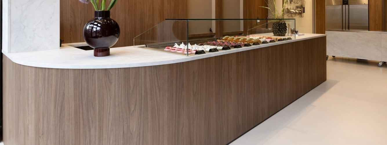 winkelinrichting op maat met lange houten patisserie toonbank, wit marmeren blad en glazen vitrine met dessert productpresentatie in modern winkelinterieur