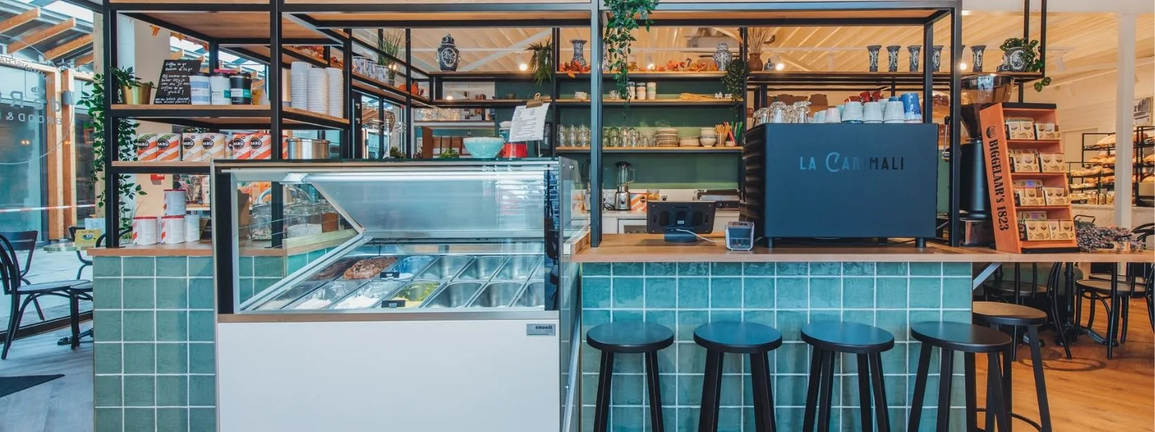 winkelinrichting op maat met groen betegelde bar, zwarte metalen stelling, ijsvitrine, koffiemachine en productpresentatie in modern horecainterieur