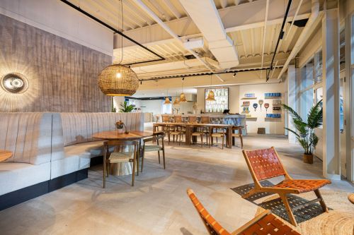 Loungehoek met maatwerk wandbank, tafels en bar in een moderne padelclub met sportkantine en clubhuisinrichting.