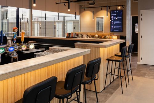 Maatwerk bar met houten afwerking en barkrukken in een moderne sportkantine van een commerciële padelclub.