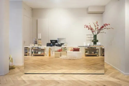 Minimalistische retail winkelbalie met spiegelend front, houten visgraatvloer en decoratieve accessoires zoals vazen, kaarsen en bloemen.