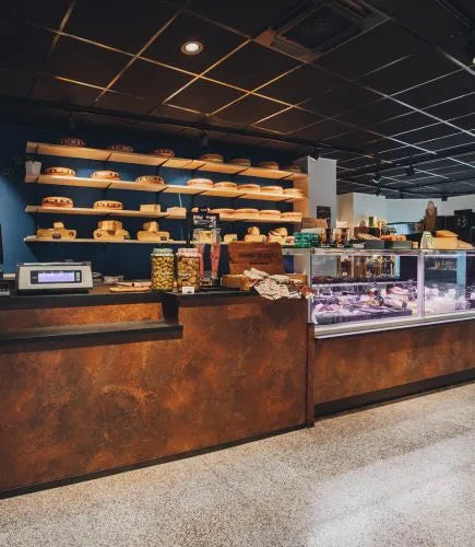 winkelinrichting op maat met roestkleurige toonbank, glazen kaasvitrine, wandplanken met kaasproductpresentatie en modern speciaalzaak winkelinterieur