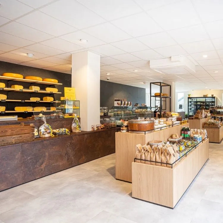 winkelinrichting op maat met roestkleurige toonbank, houten presentatiemeubel, kaasproductpresentatie op wandplanken en modern kaaswinkel winkelinterieur