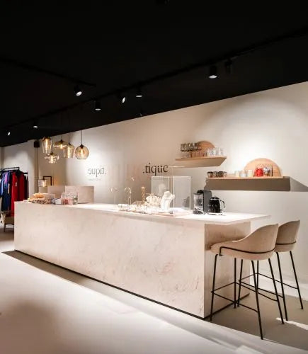 Moderne, retail winkelinrichting met een licht marmeren balie, barkrukken, hanglampen en open wandplanken met servies en accessoires.