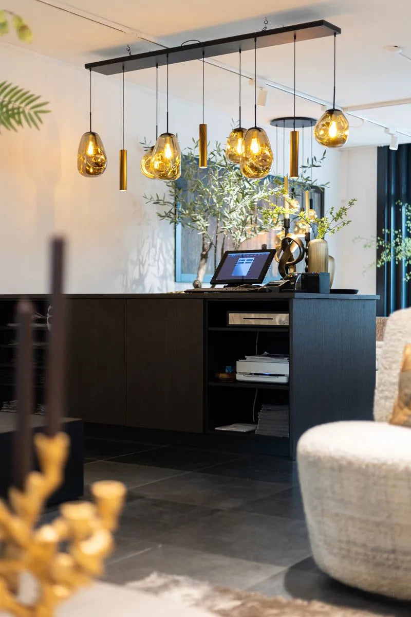 Moderne receptiebalie met donkere afwerking, sfeervolle hanglampen met warm licht, een kassasysteem op de balie en stijlvolle decoratie met planten in een luxe interieur.