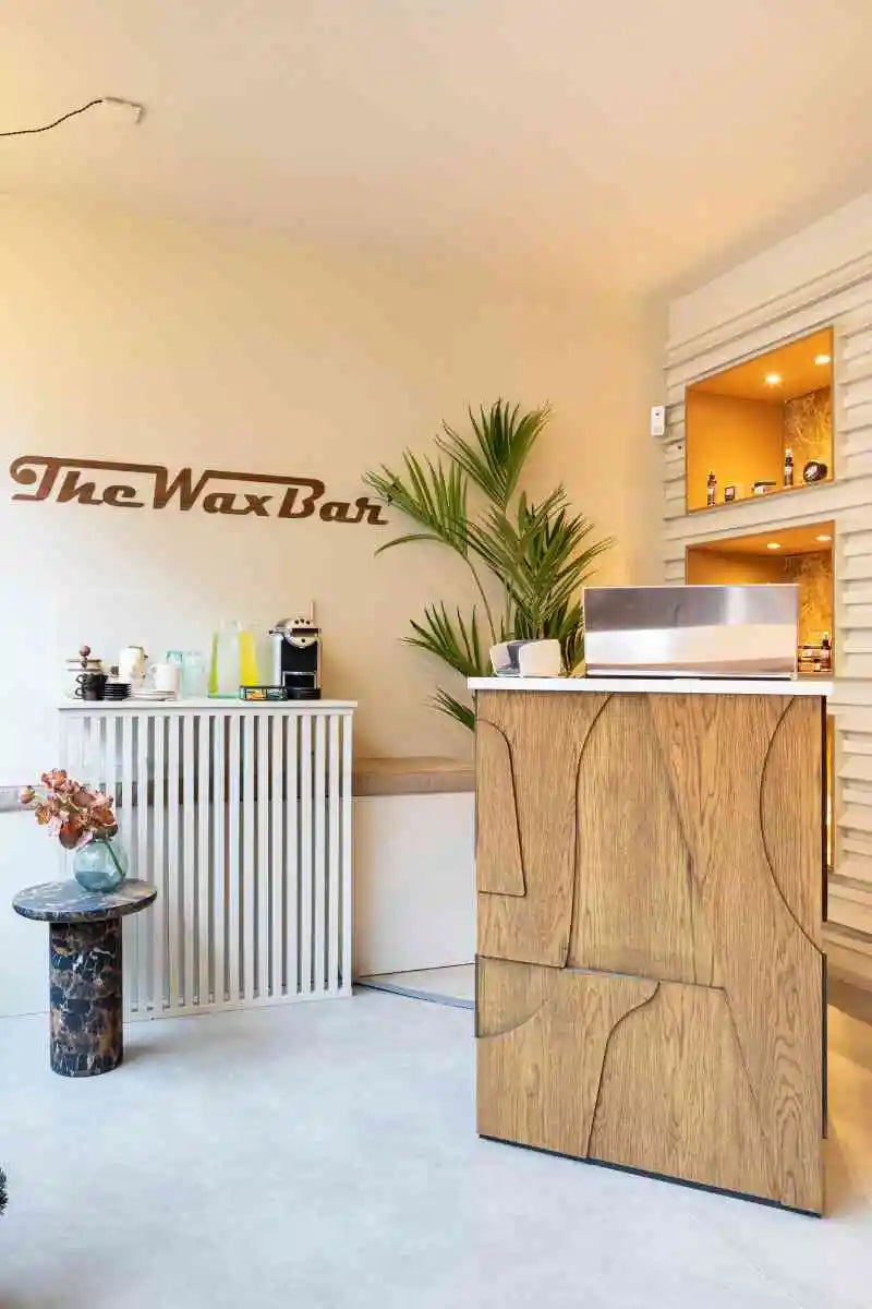 winkelinrichting op maat met houten receptiebalie, lattenwand, planten en modern saloninterieur bij The Wax Bar